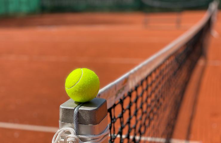 Pallina da tennis in equilibrio su un supporto della rete in un campo in terra rossa