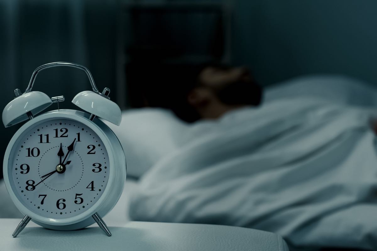 Una persona dorme con una sveglia in primo piano